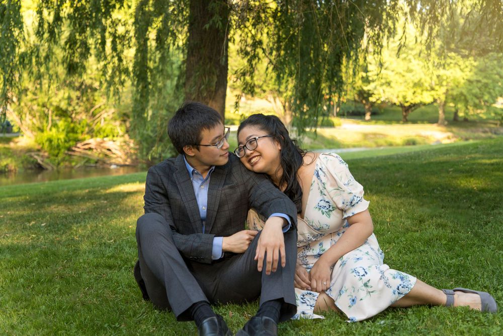 A couple sitting on the grass under a willow tree cuddled into one another