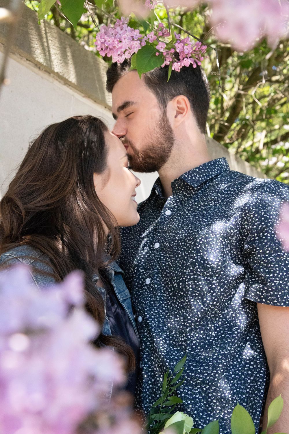 a couple with the guy kissing the girls forehead with purple flowers in the foreground