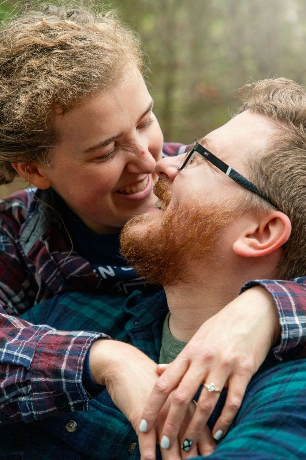 a Man looking up at his Fiance whose wrapped her arms around his shoulders behind him leaning in for a kiss