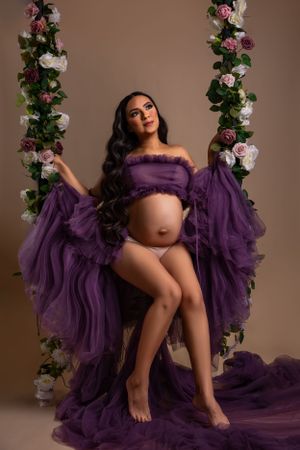 Maternity portrait with purple tulle dress and floral arch decorated with pink and white roses.