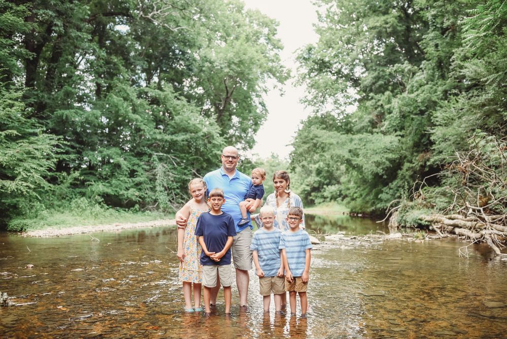 Family standing together in shallow creek water surrounded by lush greenery.