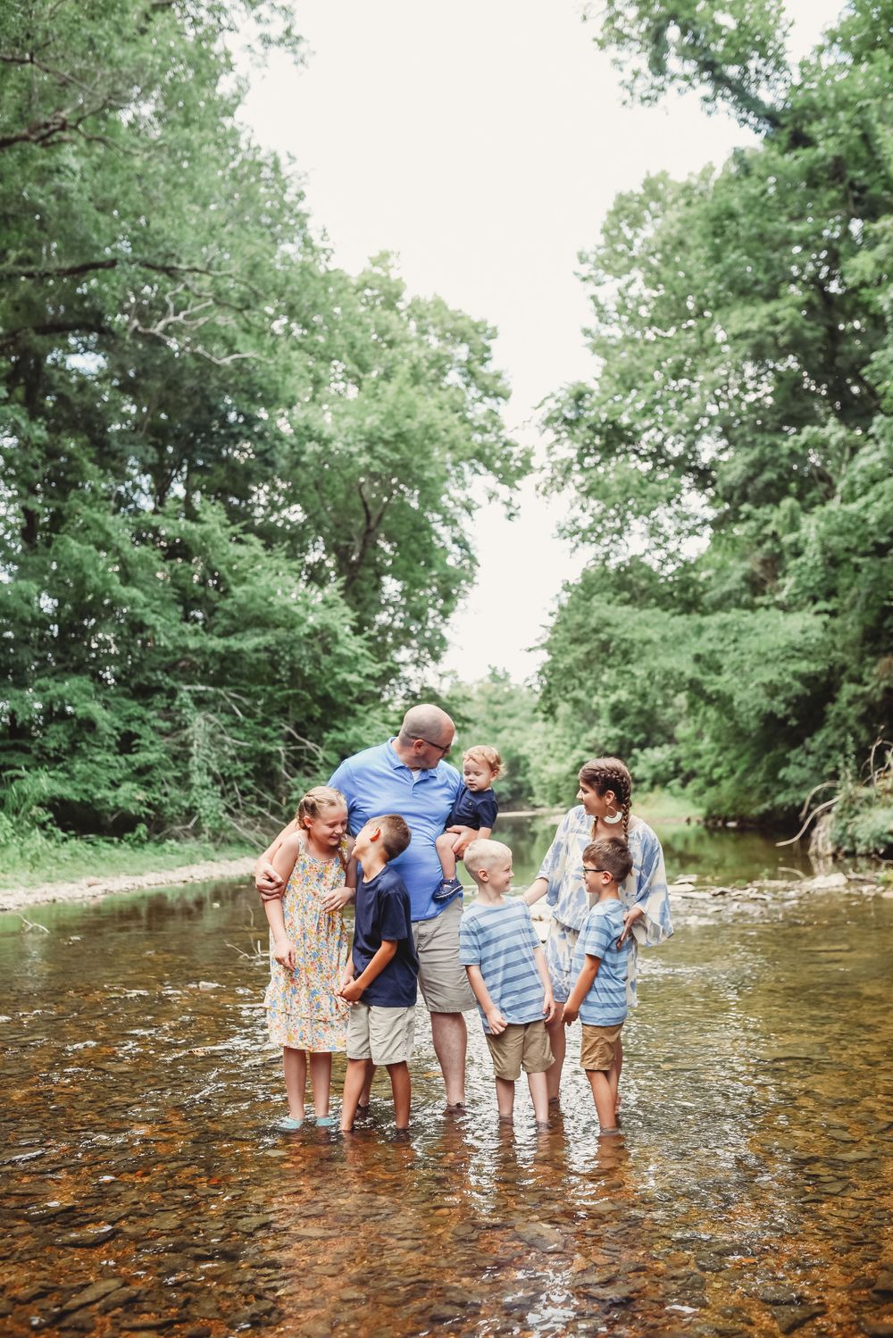 Group enjoying summer day wading in shallow river surrounded by trees.
