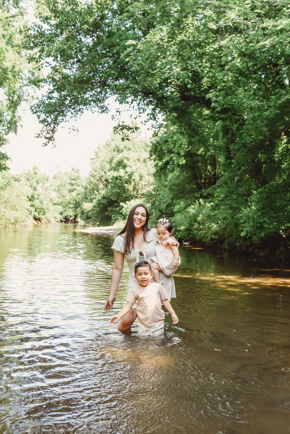 People enjoying summer day wading in shallow river water under tree canopy.