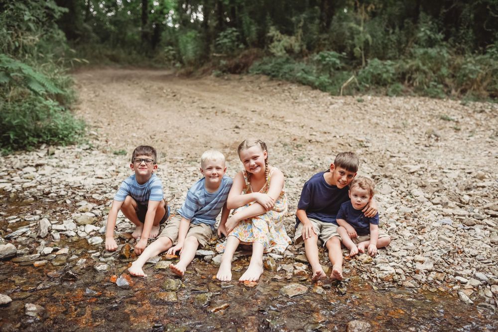 Kids lying on their stomachs on a rocky riverbank during an outdoor adventure.