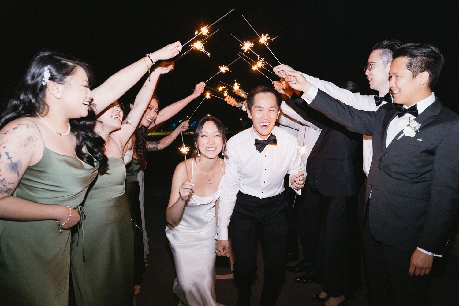 Party guests dancing and celebrating under string lights at a nighttime wedding reception.