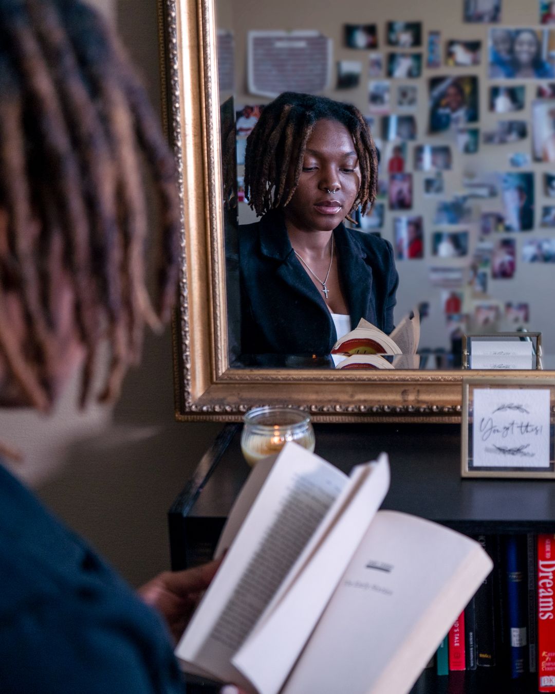 Reflective scene of person reading book while looking in ornate framed mirror.