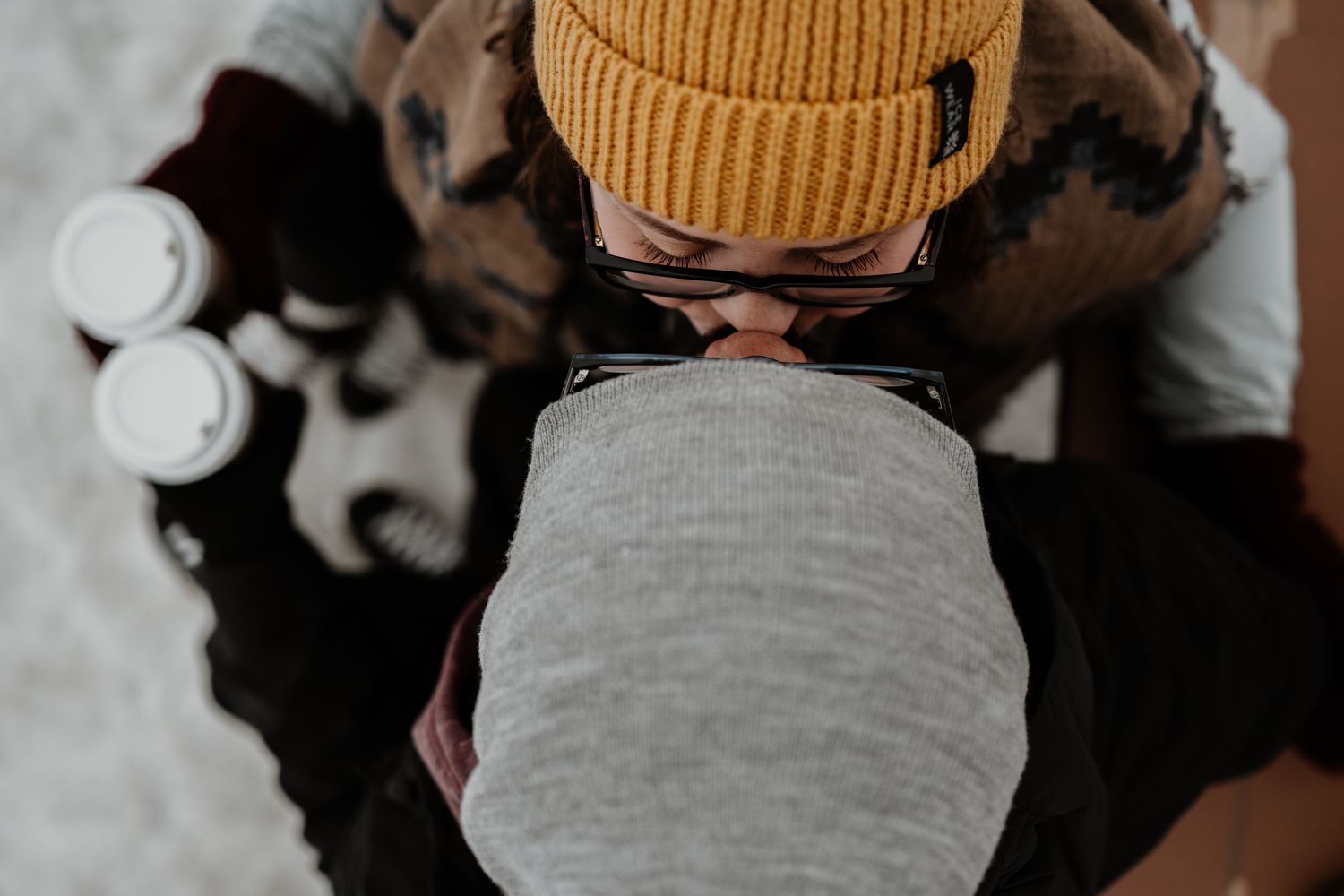 Person wearing a yellow beanie hat holds white baby bottles while looking down at a black and white object.