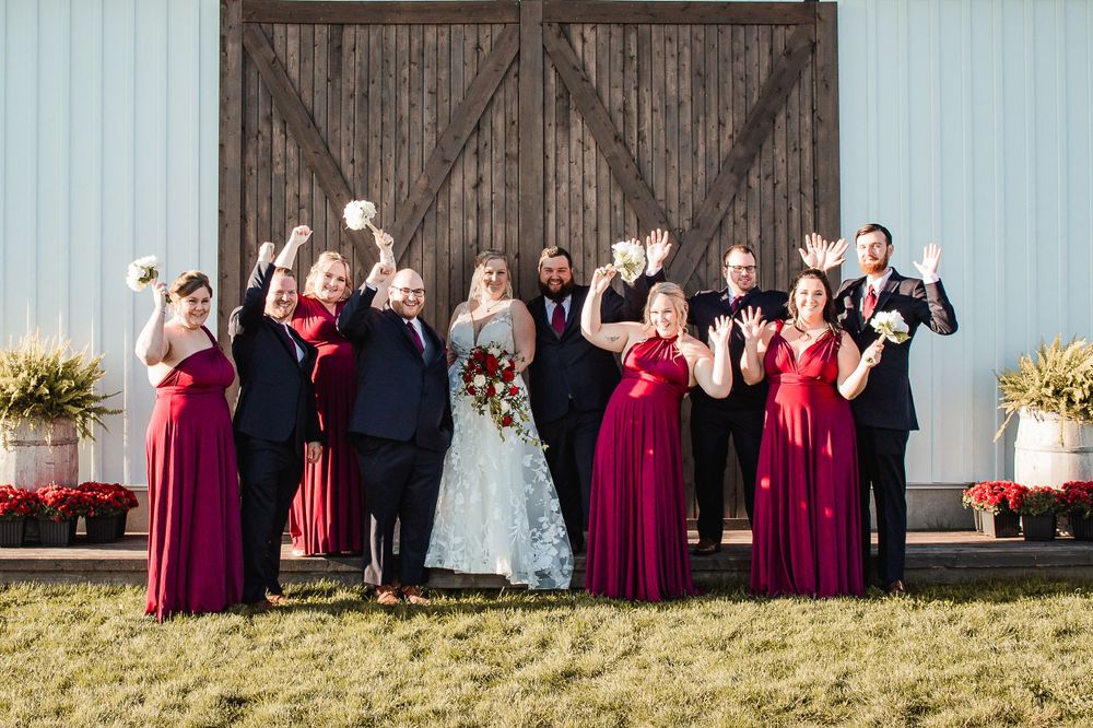 Wedding party poses playfully with raised hands in front of rustic barn doors.