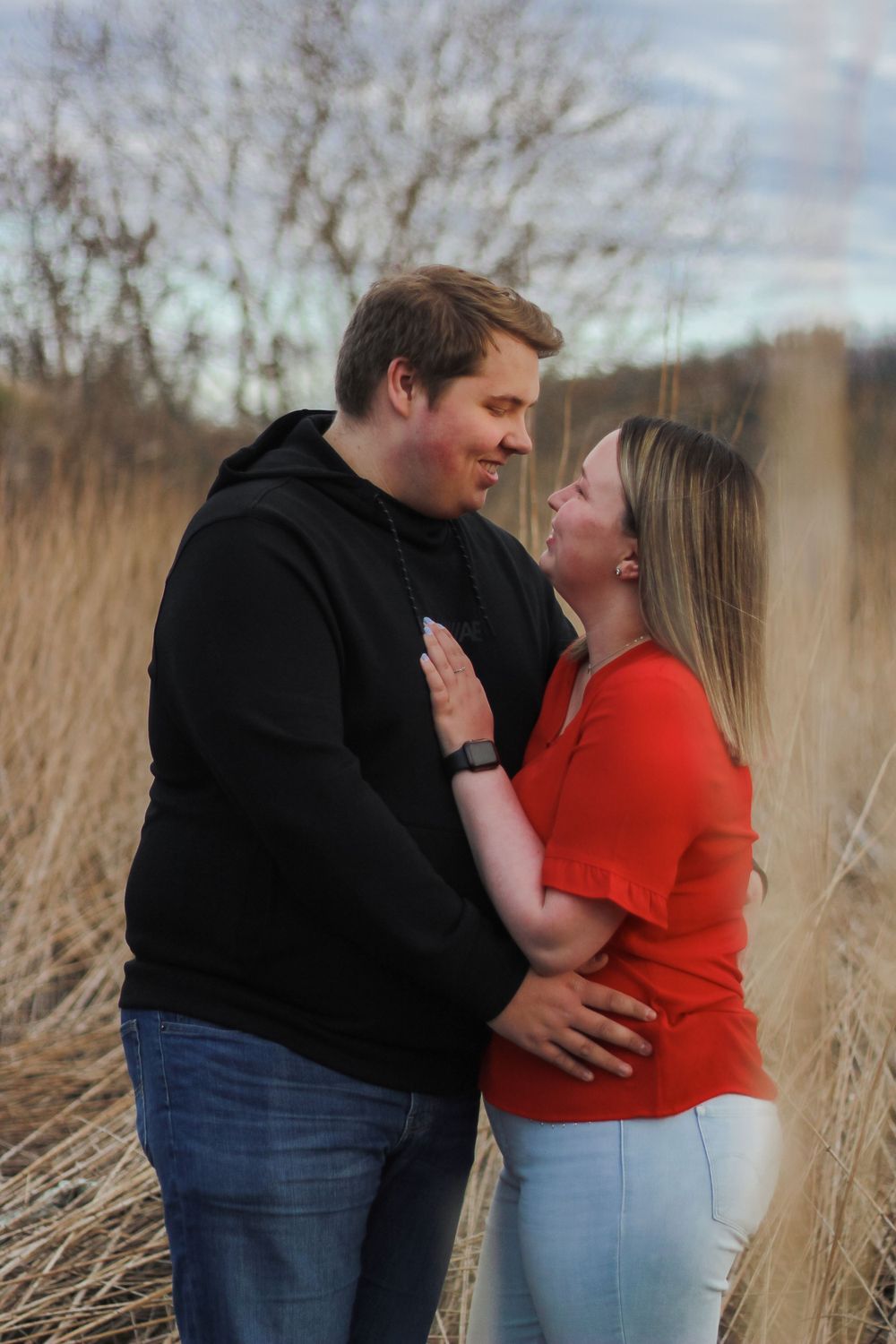 Intimate couple embracing in a field of dried grass during golden hour.