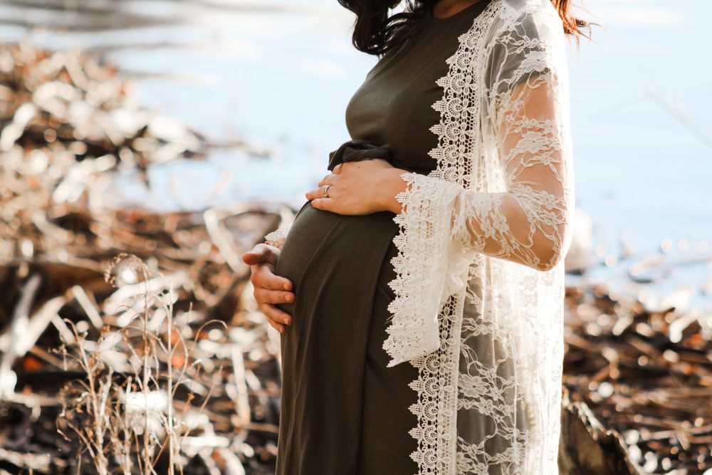 A detailed shot of a pregnant belly with delicate lace overlay against a lakeside backdrop.