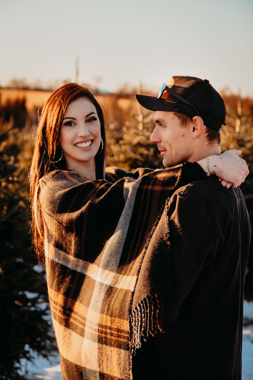 Couple shares intimate moment wrapped in plaid blanket during sunset.