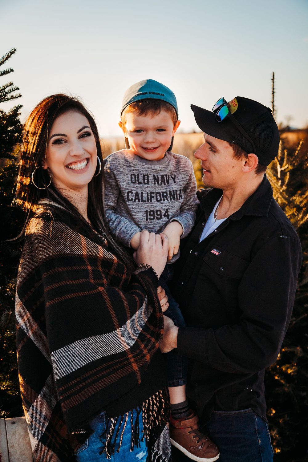 Family of three smiling together outdoors during golden hour sunset.