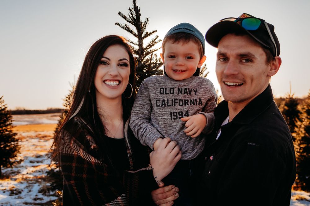 Happy family poses together near evergreen trees during sunset.