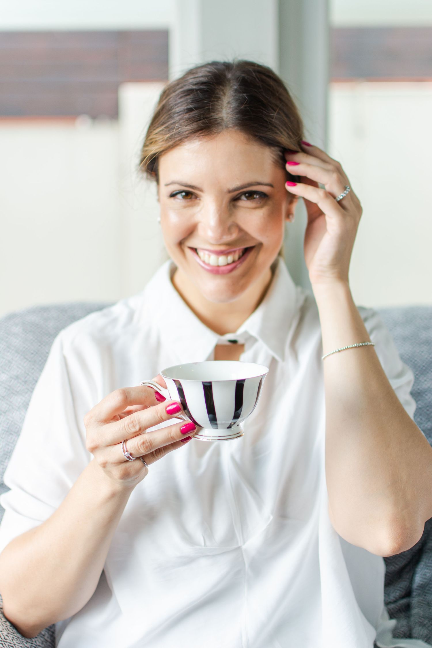 Portrait with striped teacup shows bright manicure and delicate bracelet accessory.