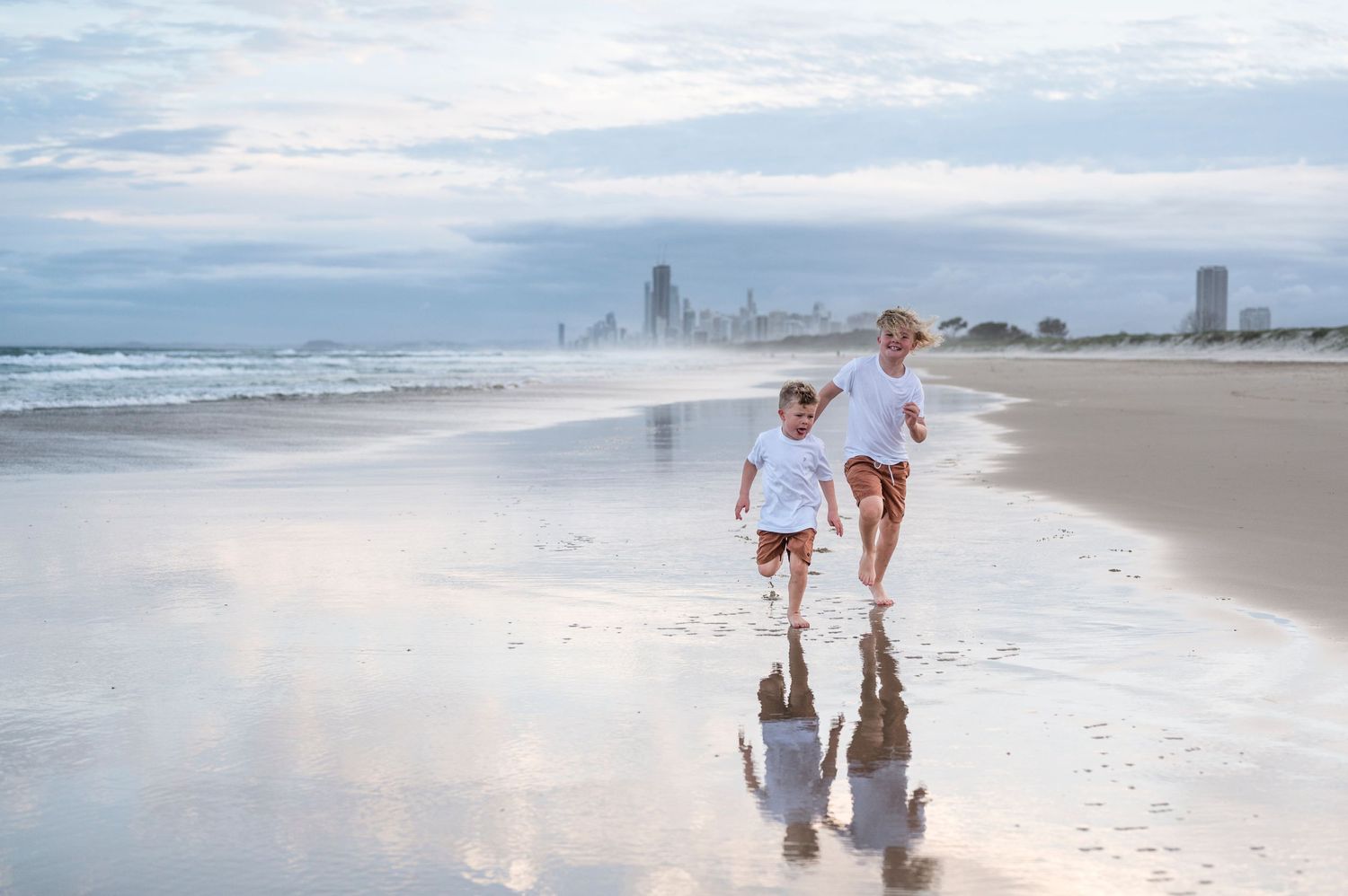 Mother and child running along reflective beach shoreline at dusk.