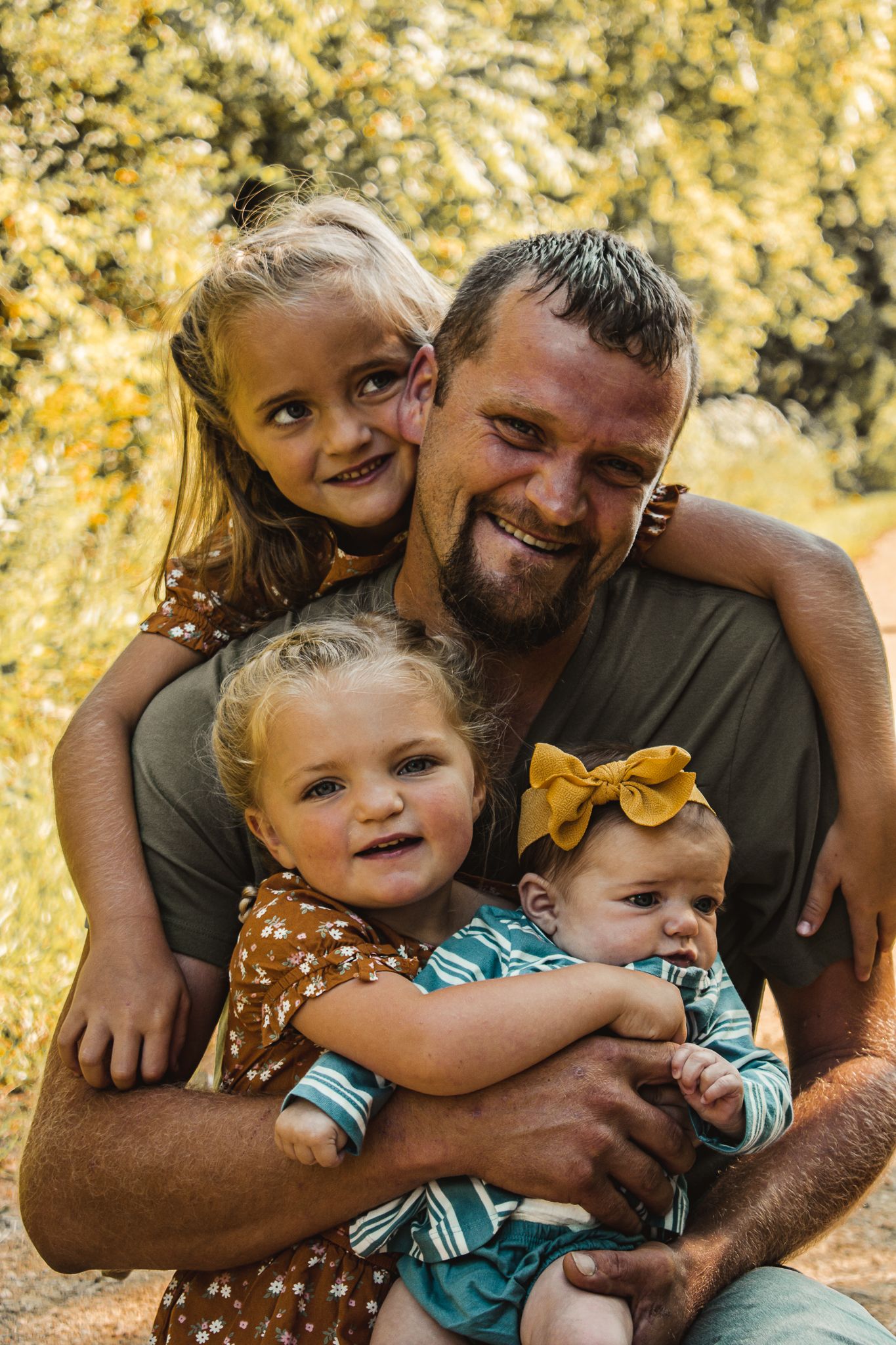 A joyful outdoor family portrait with warm yellow bokeh background.