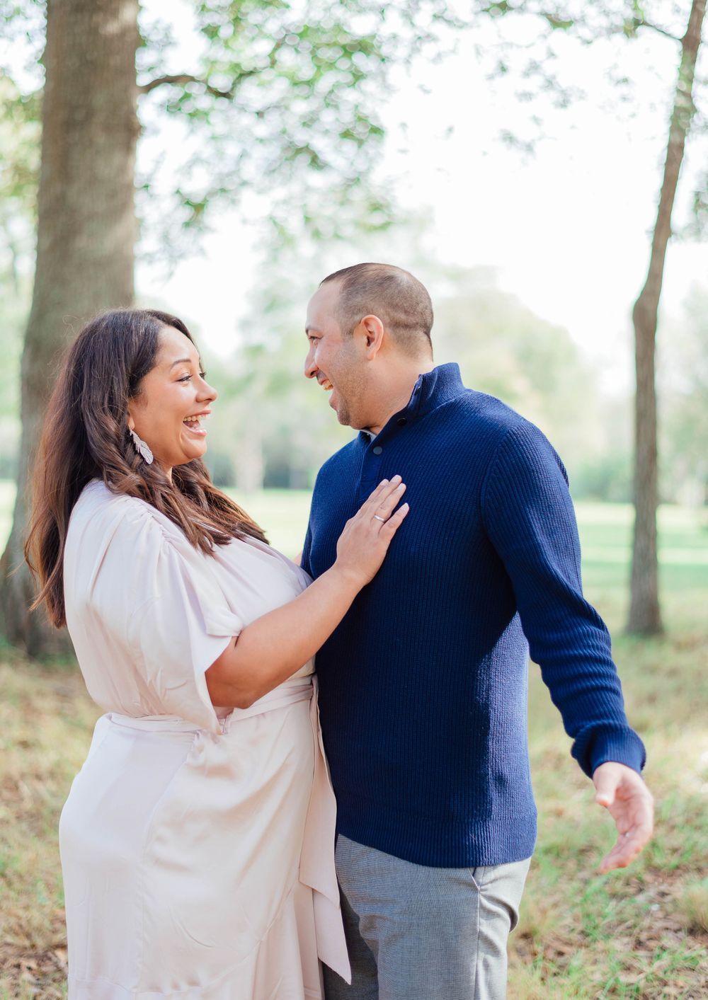 A loving couple laughing together during an outdoor portrait session wearing coordinated blue and white outfits.