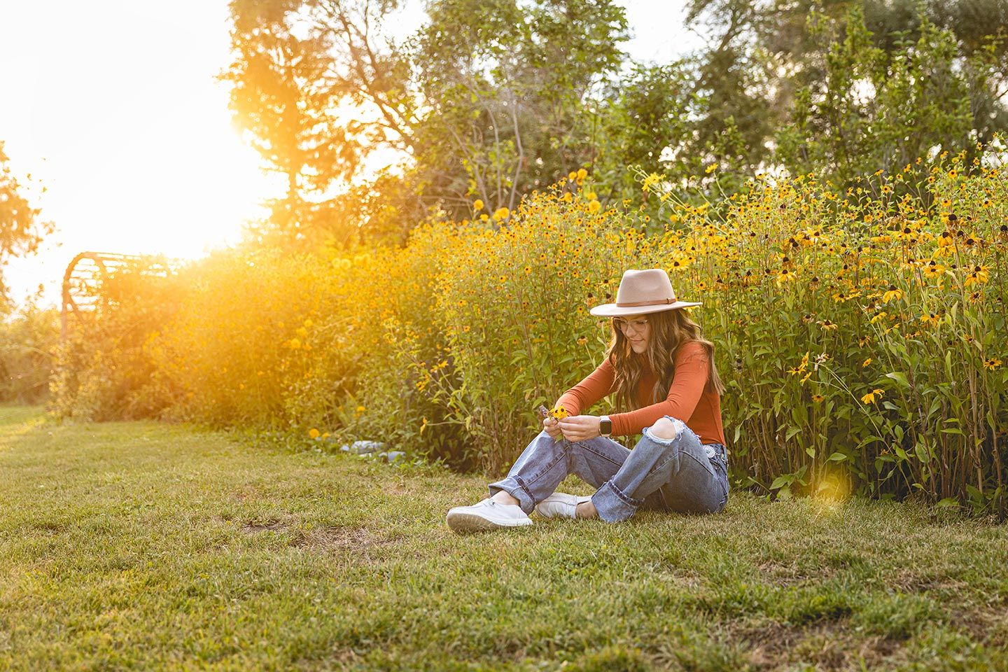 high school senior girl sitting in the grass next to tall flowers in kittitas county, WA