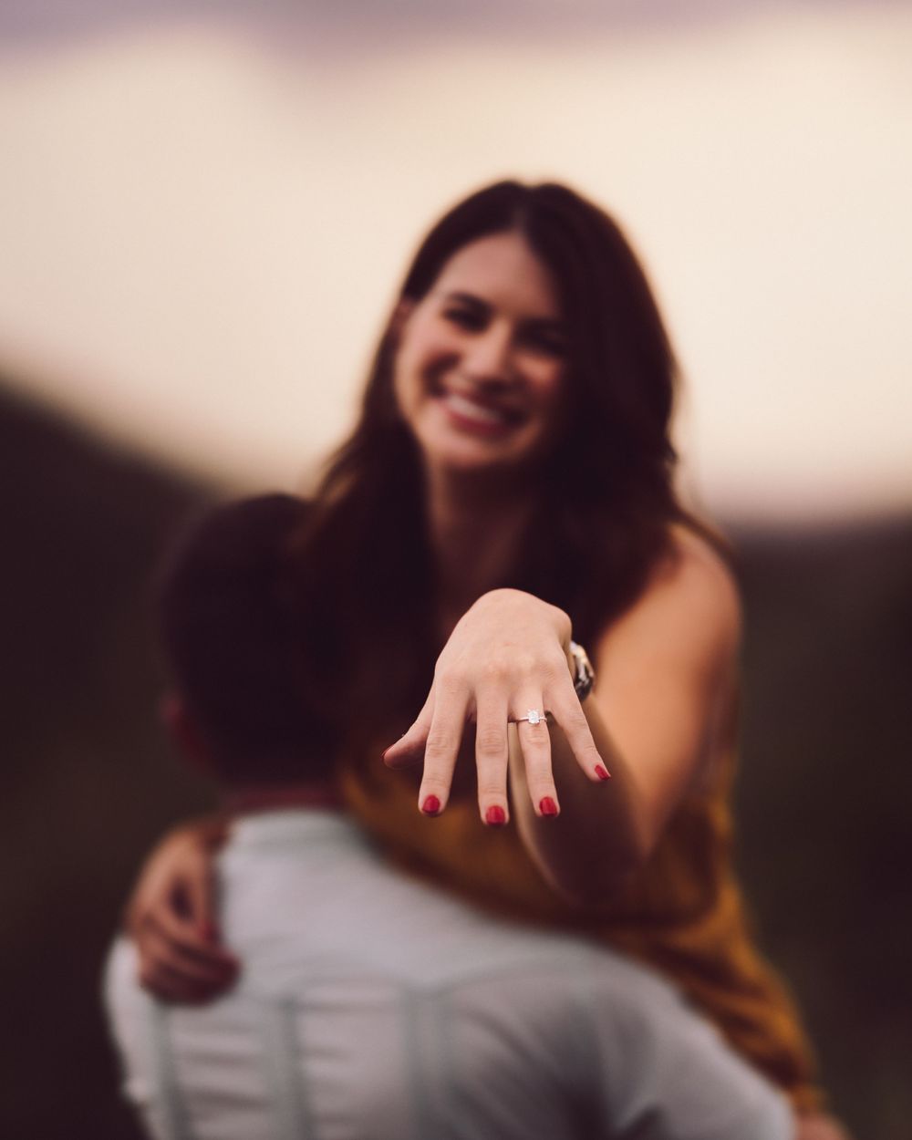 Woman shows off her engagement ring while being held up by her future husband