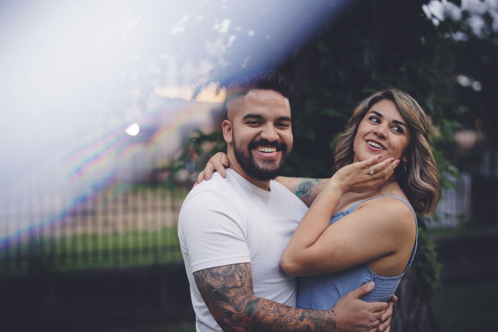 Bride to be shows off her engagement ring while future groom smiles at camera