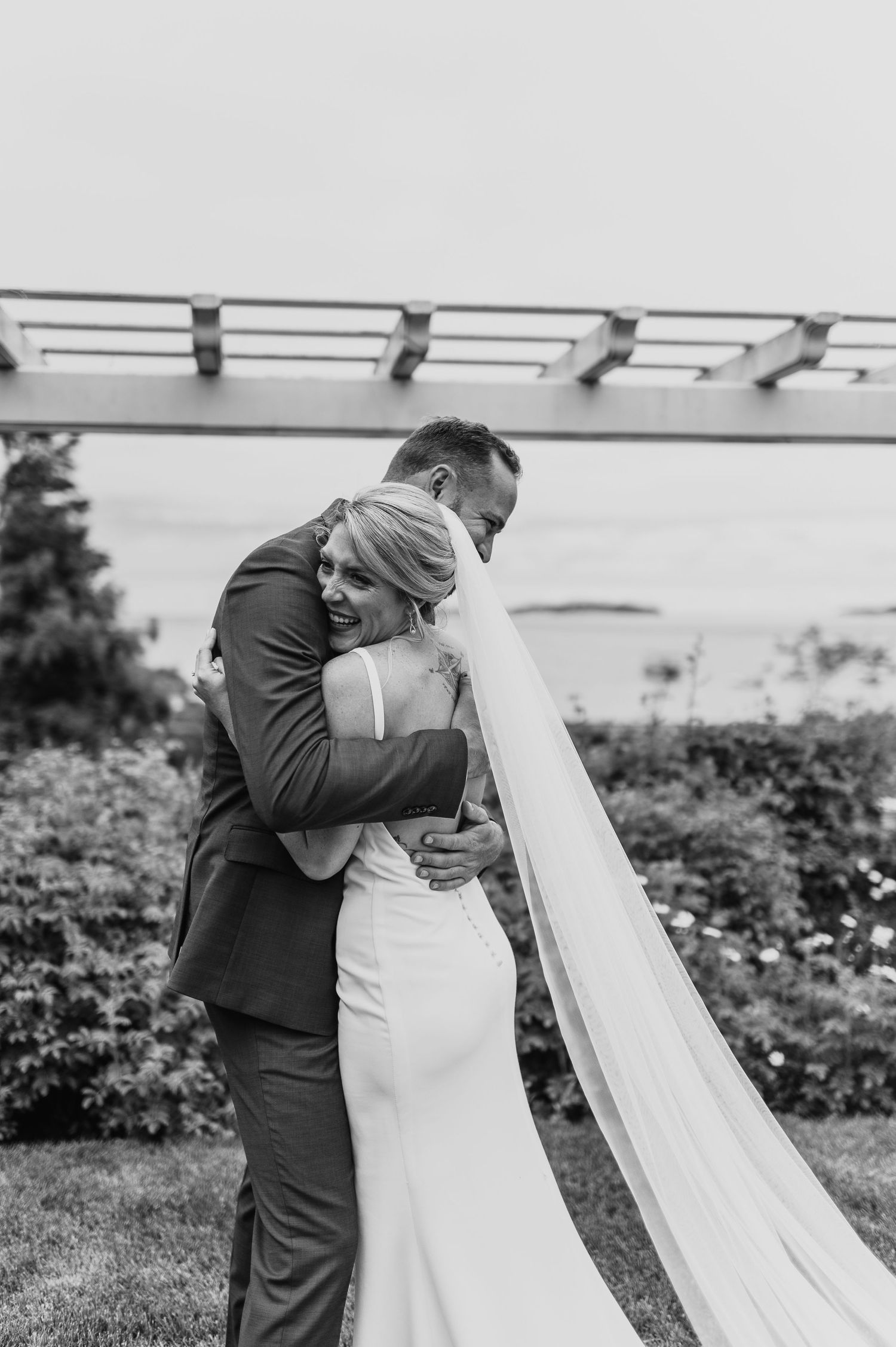 A tender black and white wedding portrait under a pergola showing an intimate embrace.