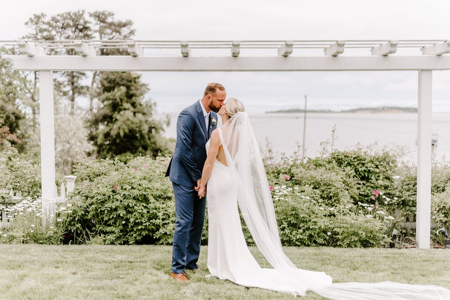 A romantic wedding moment under a white pergola overlooking a scenic waterfront view.