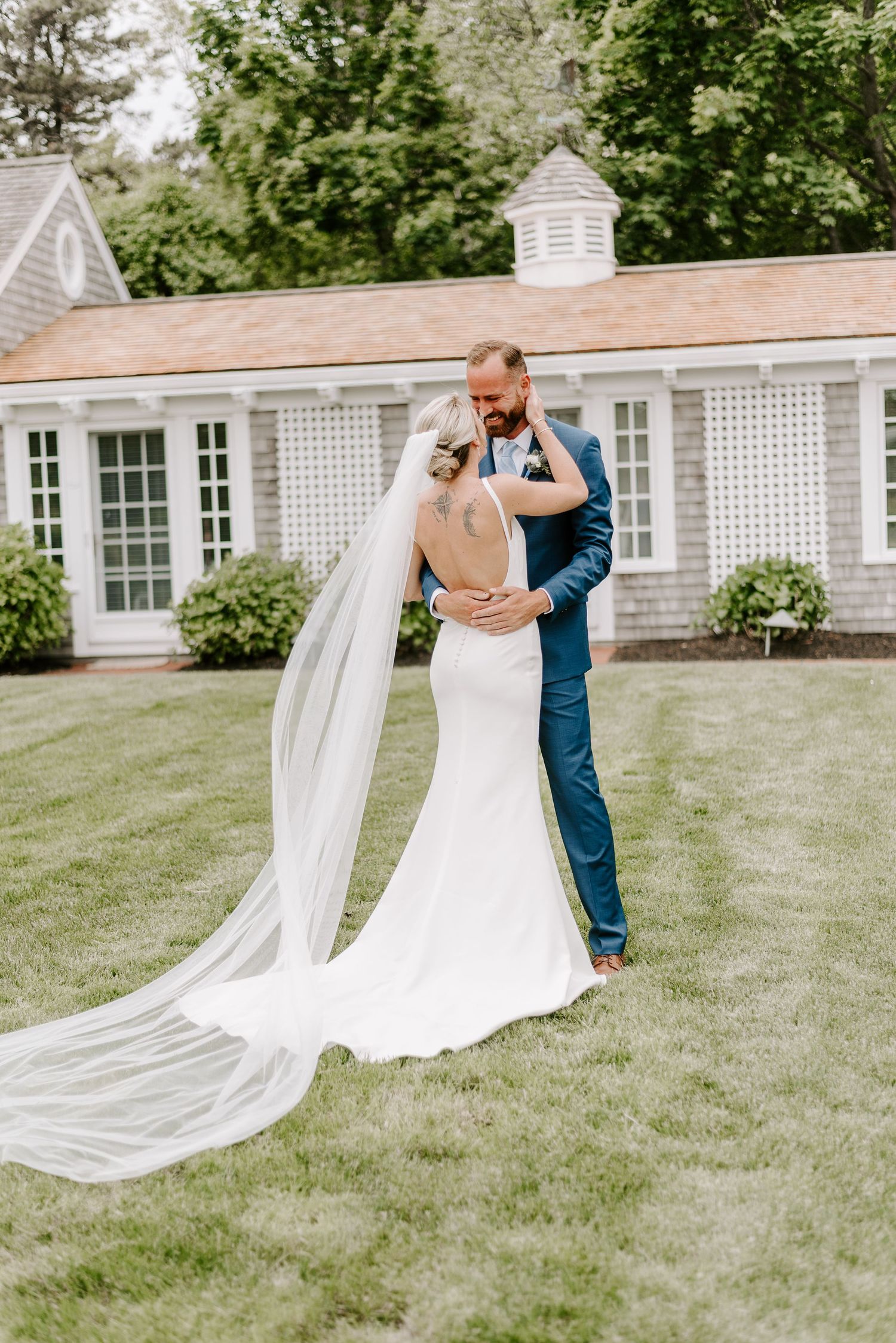 A romantic wedding moment captured on a lawn with a beautiful white building and lattice windows in the background.