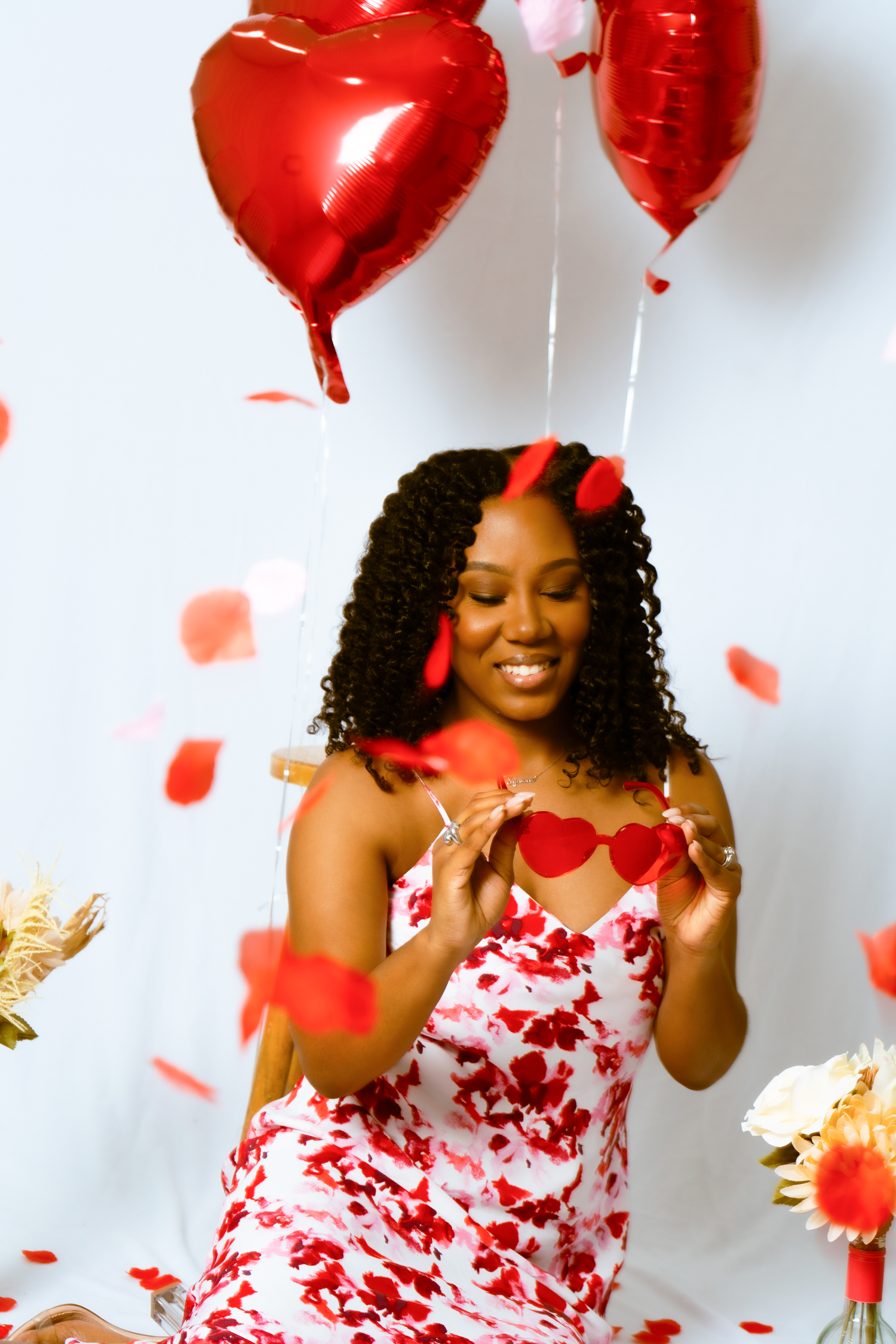 Young woman holding heart shaped glassed while red petals fall around her