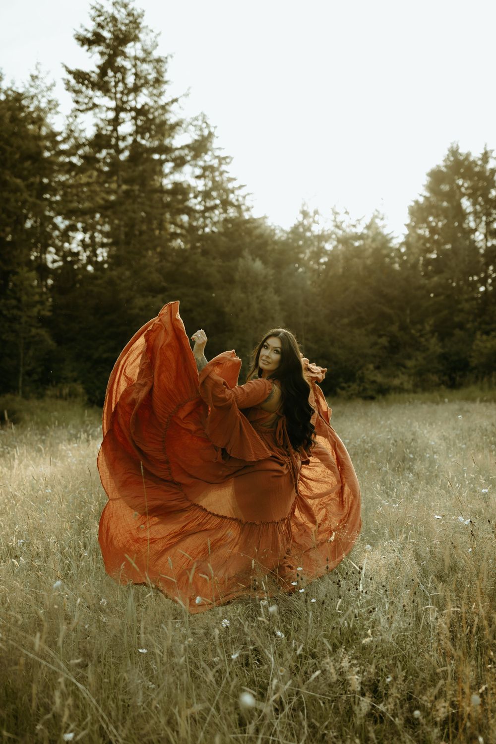 Flowing rust-colored dress swirls dramatically in a golden meadow at sunset.
