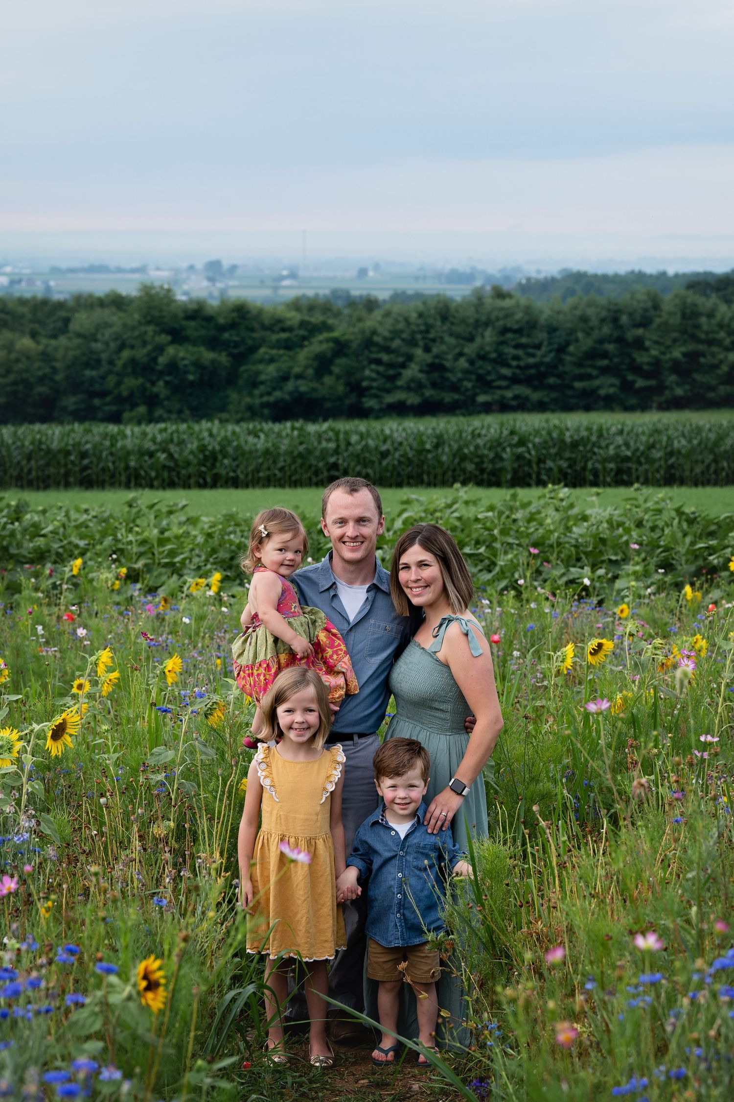 A family stands together in a vibrant wildflower meadow with mountains in the background.