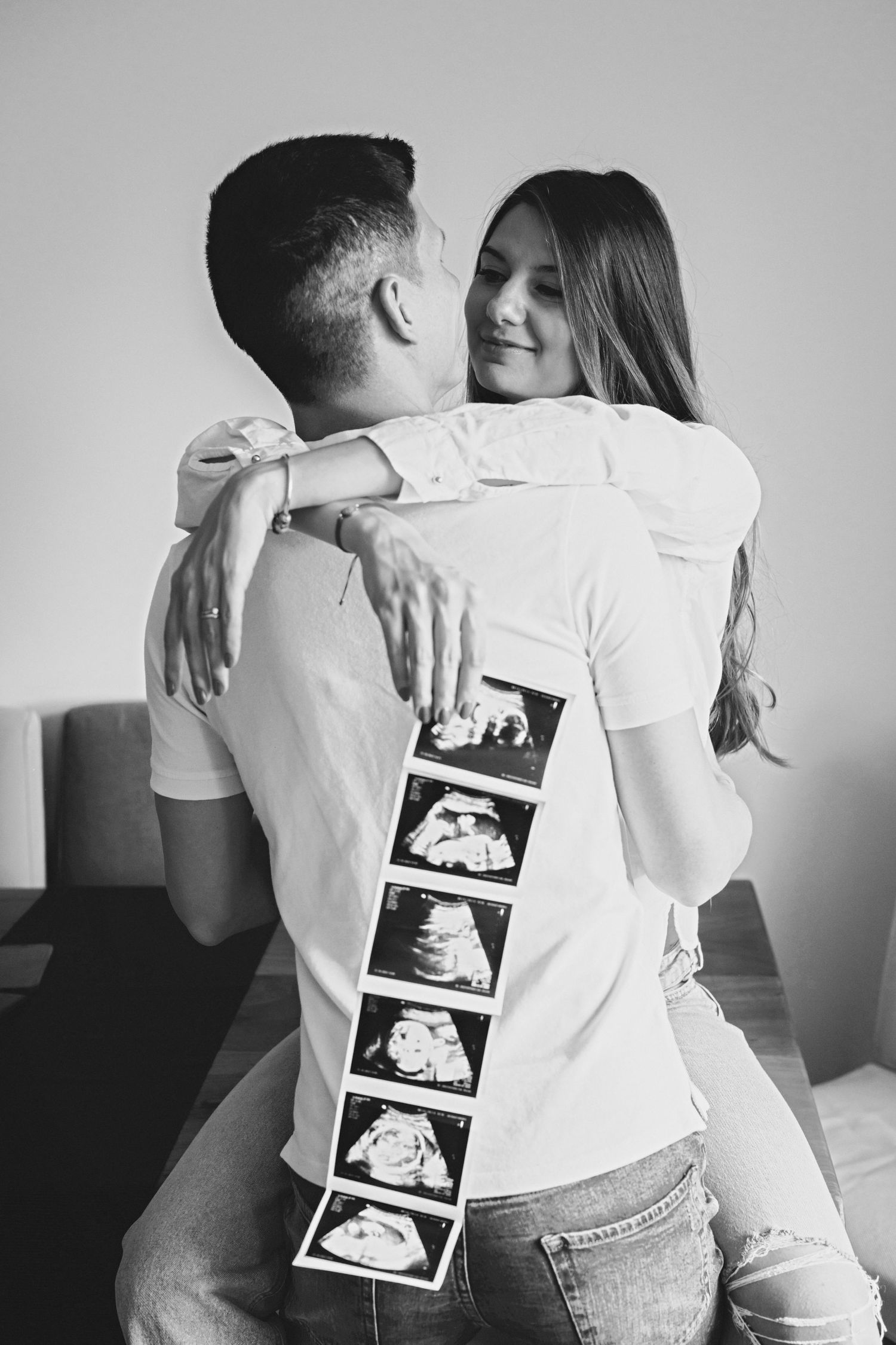 Couple embracing while holding ultrasound photos showing pregnancy announcement.