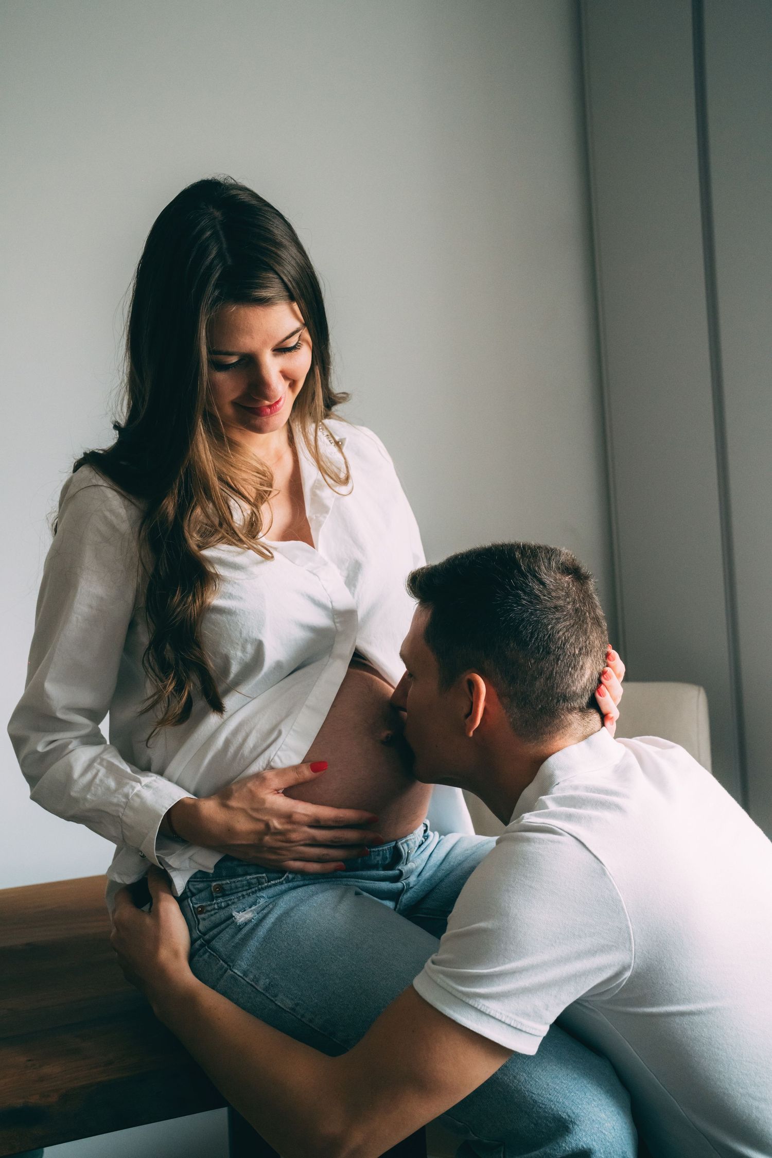 Intimate maternity photo with couple sharing tender moment by window.