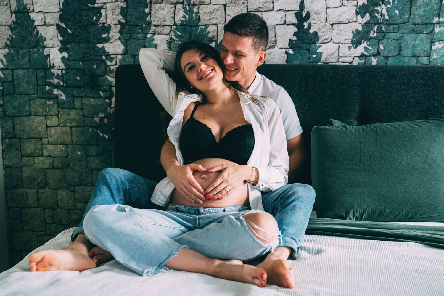Candid maternity moment showing couple relaxing on couch in casual attire.