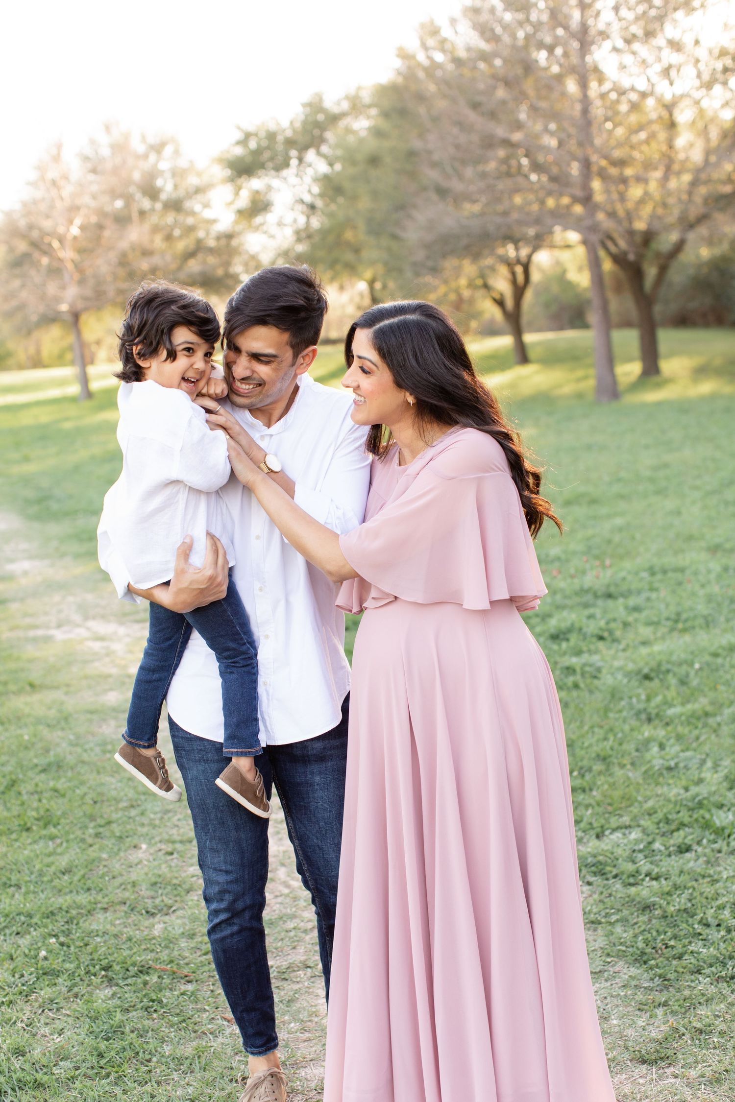 A tender family moment captured in warm sunlight with natural greenery in the background.