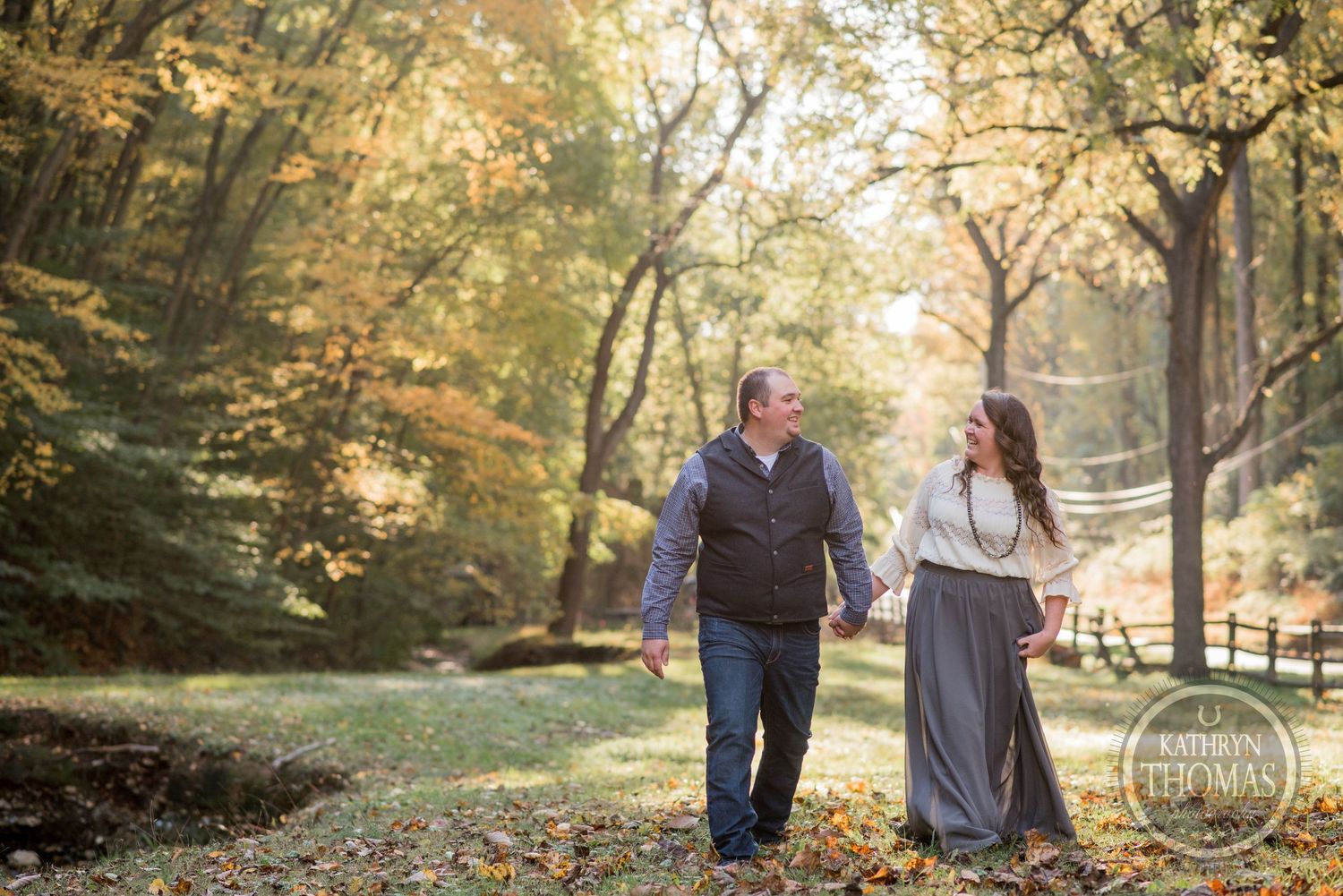 A couple strolls hand in hand through an autumn forest path with golden leaves.