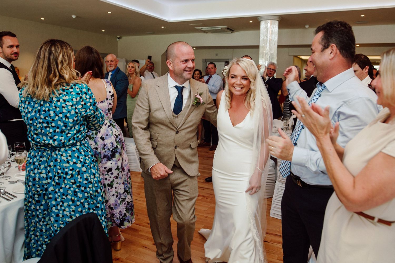 Wedding reception celebration with guests applauding in an elegant indoor venue.