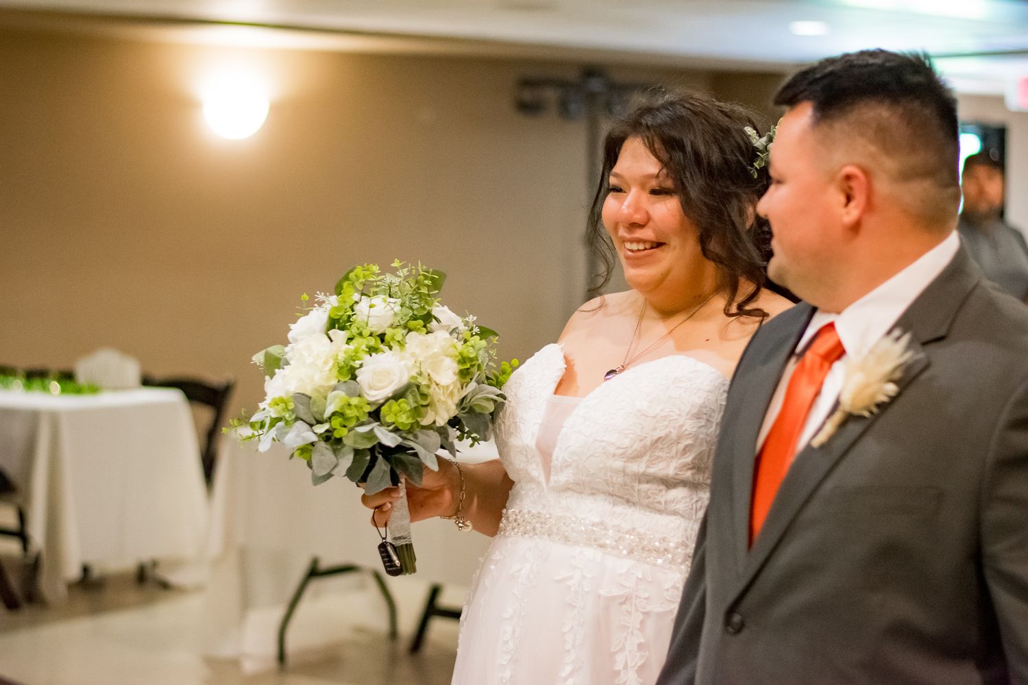 Wedding couple holding bouquet with white flowers and greenery indoors.