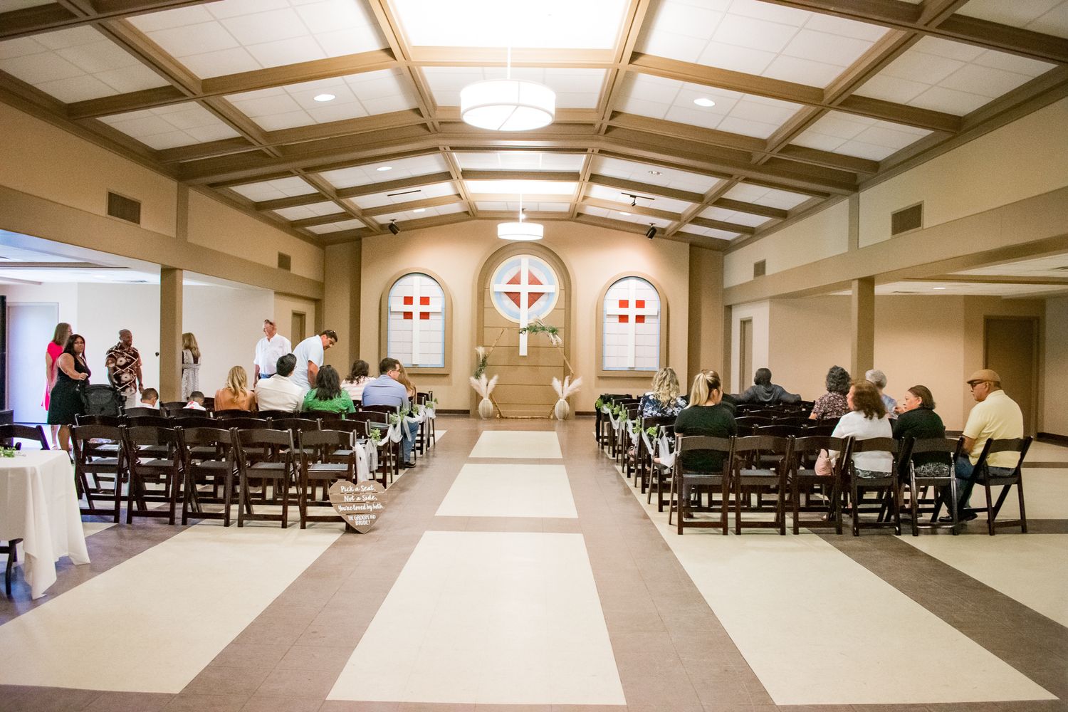 Interior of a church venue with cross-adorned windows and rows of dark chairs for a wedding ceremony.