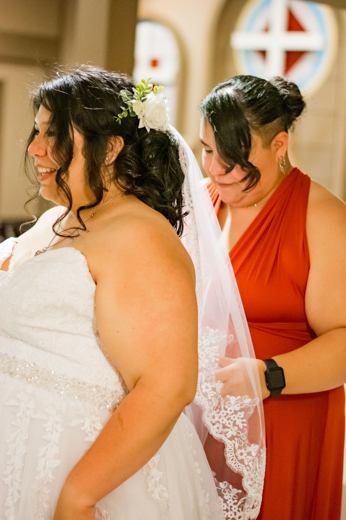 A tender wedding moment between a bride in white lace and bridesmaid in red.