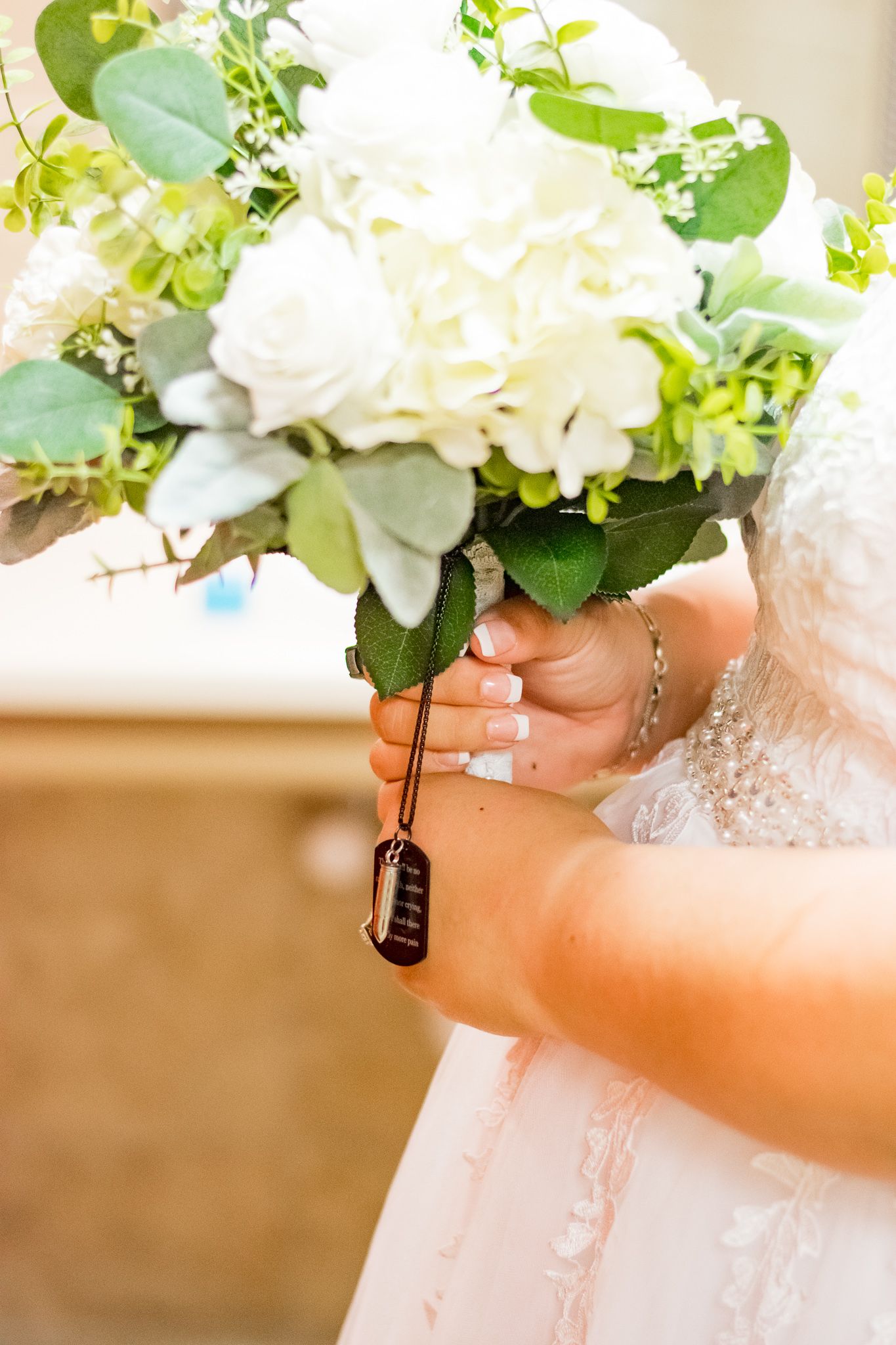 A bridal bouquet of white roses and greenery held with a decorative charm.