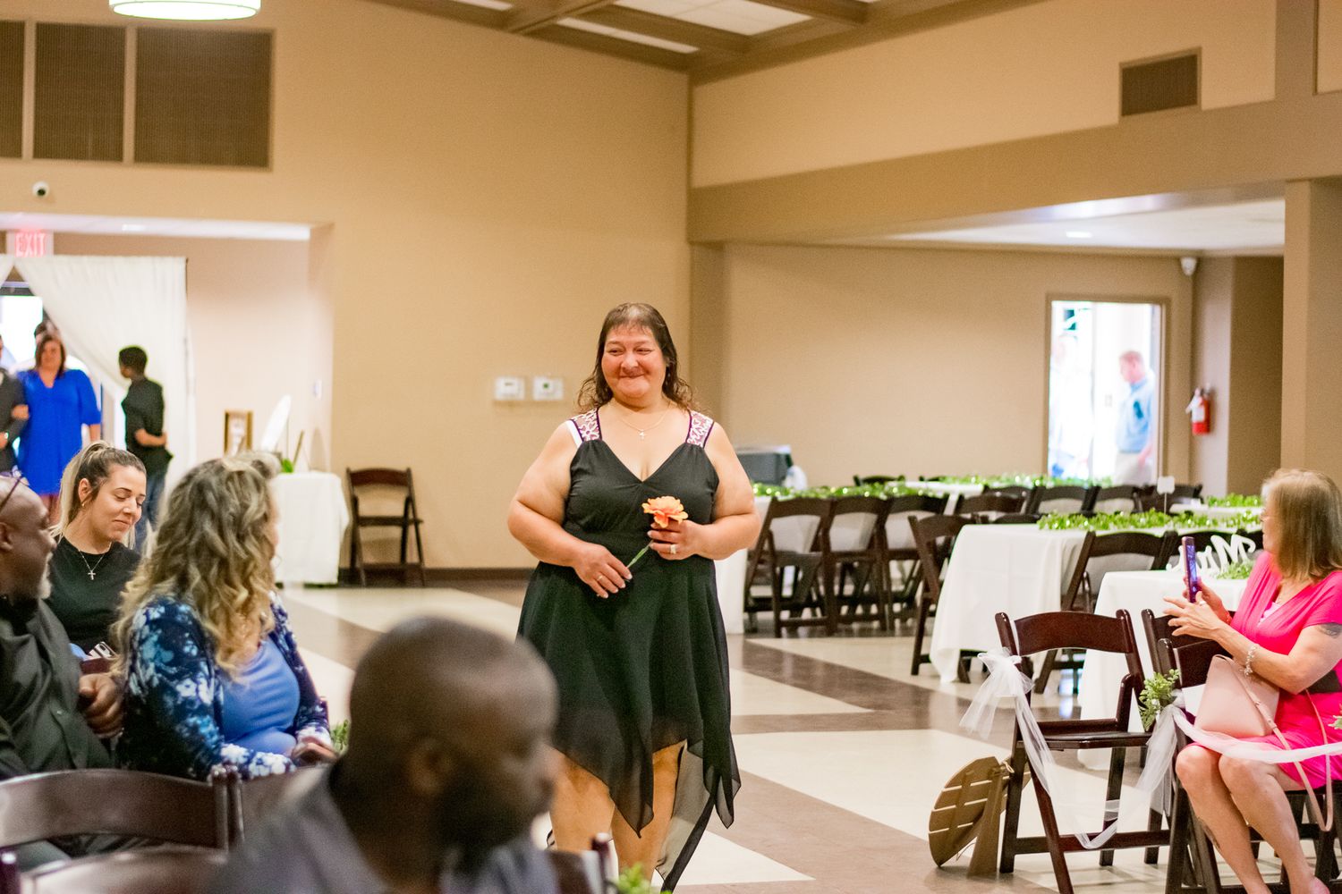 Person in green dress speaking to seated guests at an indoor wedding ceremony venue.