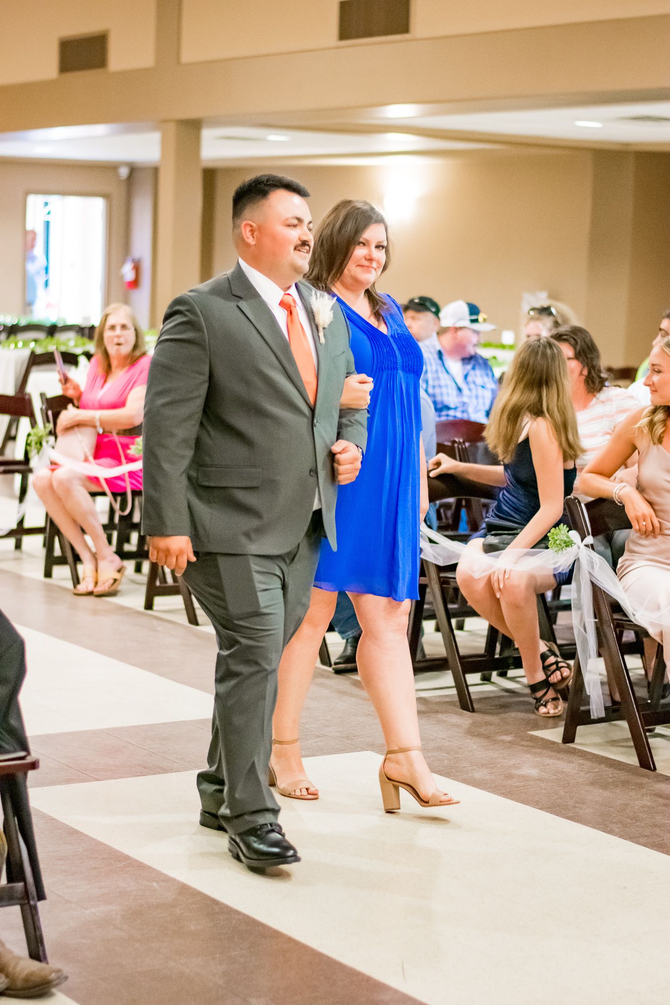 Couple walking down aisle at wedding reception, with man in suit and woman in blue dress.
