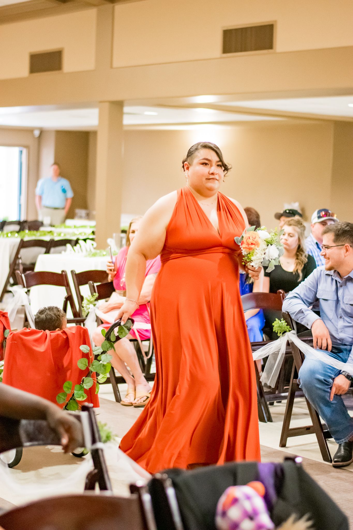 Person in elegant orange halter dress holding bouquet during wedding ceremony.