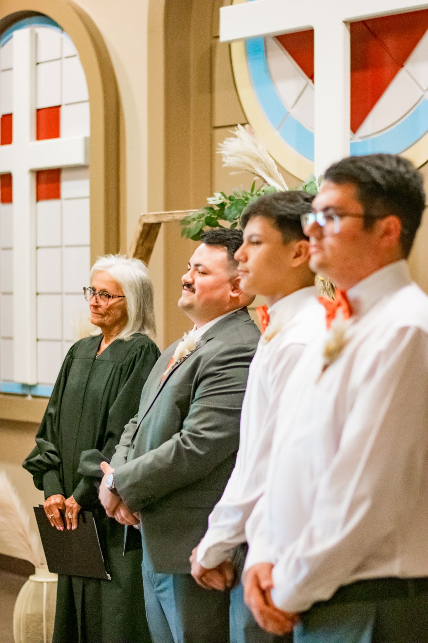 Wedding party members standing in formal attire near church archway with stained glass.
