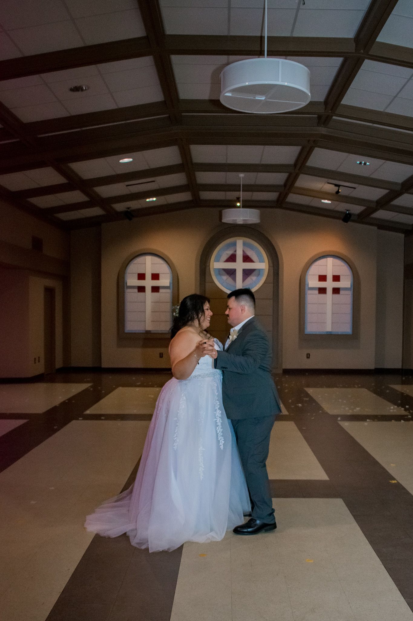Couple dancing in an elegant church hall with decorative arched windows.