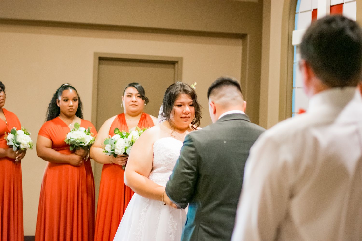 Wedding ceremony with bridesmaids in orange dresses standing at altar.
