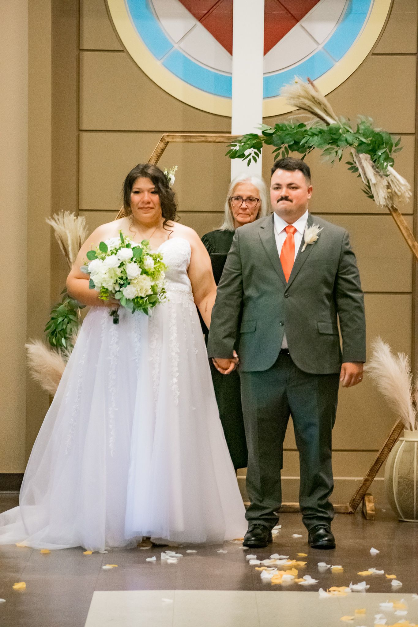 Wedding ceremony in front of a circular window with a bride in white dress and groom in gray suit.