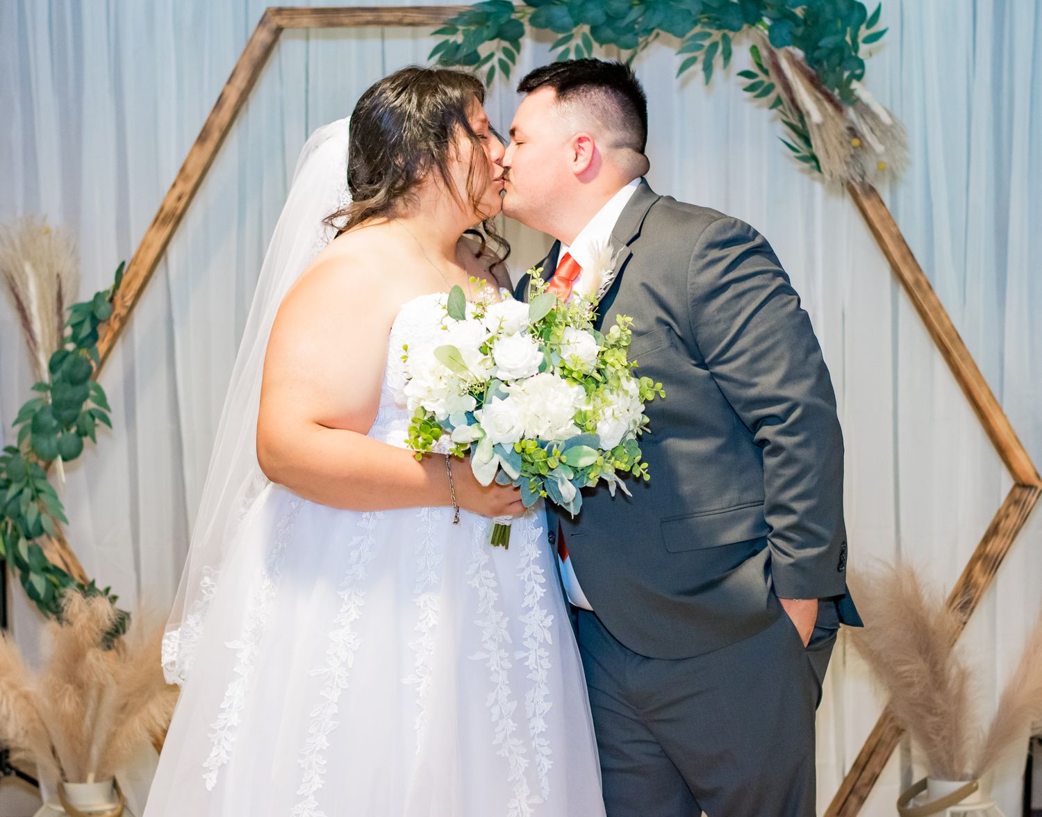 Candid moment between newlyweds under a geometric wedding arch with white florals.
