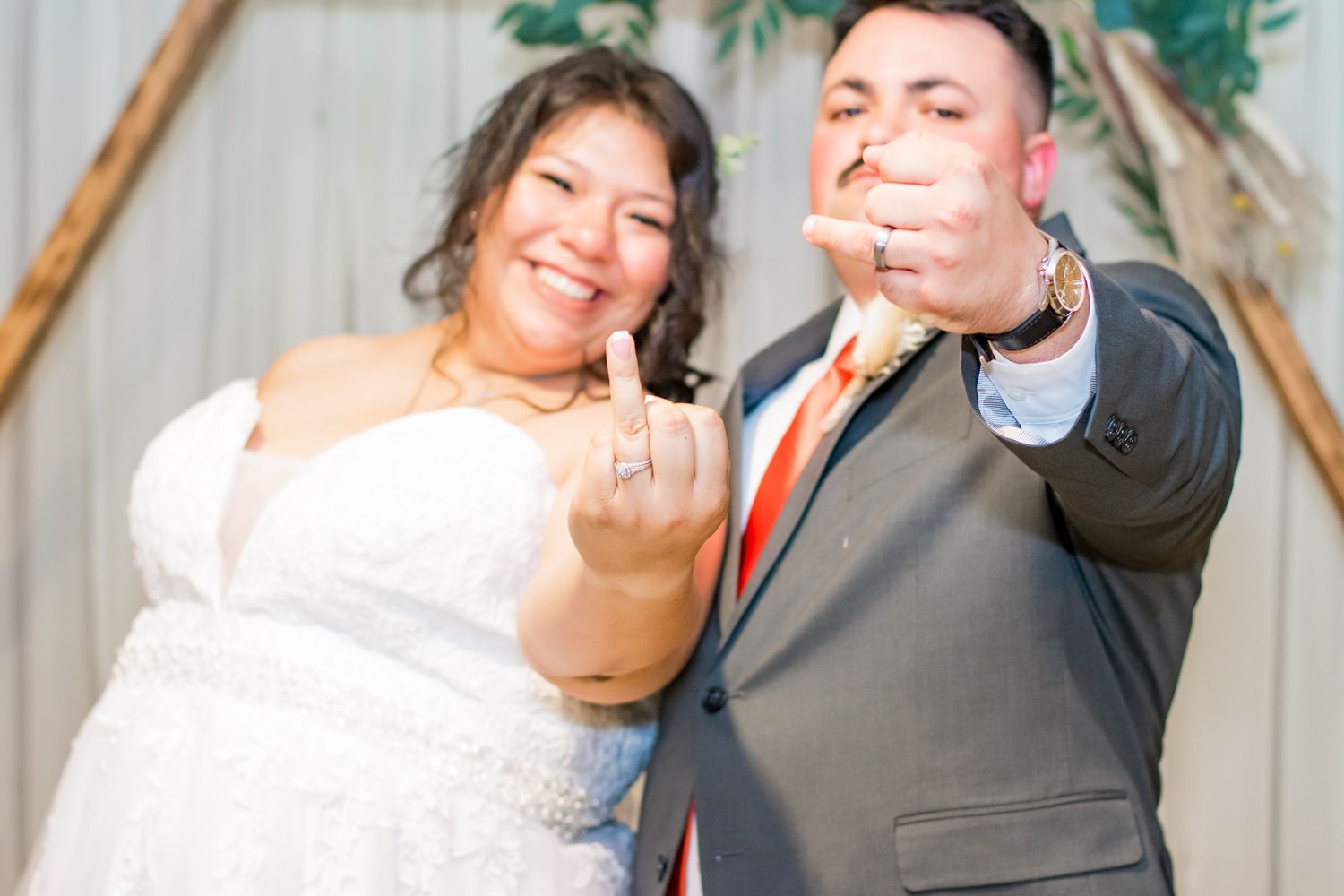 Playful wedding portrait of couple making silly faces under decorated arch.