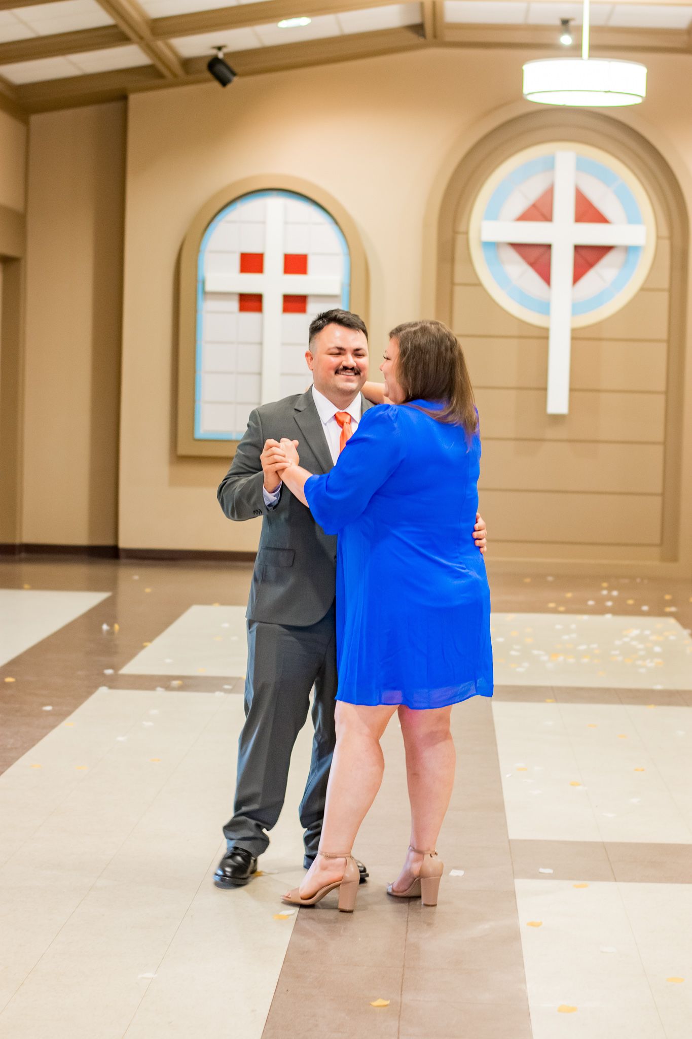Couple dancing in church hall with decorative stained glass windows.